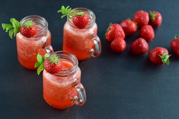 Fresh organic strawberry smoothie with mint in glass jar on black background