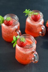 Fresh organic strawberry smoothie with mint in glass jar on black background
