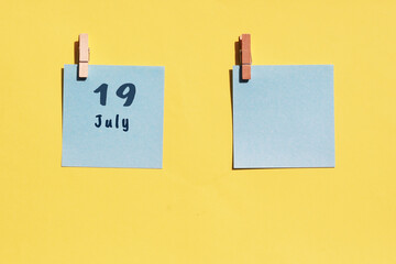 July 19st. Day of 19 month, calendar date. Two blue sheets for writing on a yellow background. Top view, copy space. Summer month, day of the year concept