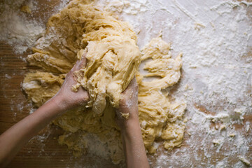 a child kneads the dough for a pie with his hands on a table covered with flour, top view