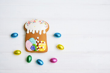 Gingerbread in the form of a cake and colorful chocolate eggs on a white wooden background.