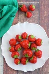 Fresh organic strawberry on white plate on wooden background