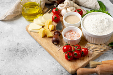 Pizza ingredients on a culinary background. Flour, yeast, salt, water, olive oil, parmesan, cheese, mozzarella, basil, tomatoes on the table. The concept of preparing for baking pizza or pie