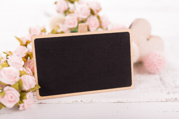 Small blank chalkboard for Valentine's or mother woman day. Background with pink roses on old wooden table.
