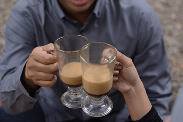 Male and female hands holding capuccino coffee drinks to toast together