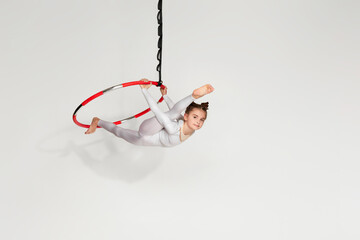 graceful little child girl gymnast in white sportwear doing twine on an aerial hoop. Acrobatics...