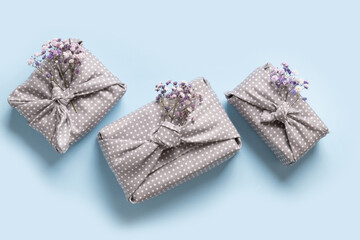 Spring eco-friendly gift wrapped in grey textile with flowers on blue. Sustainable gift. Zero waste. Traditional Japanese Furoshiki style. View from above.