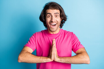 Photo of young smiling brunet arab man in pink t-shirt pray isolated on blue color background