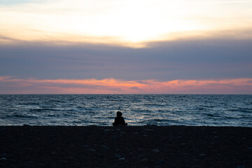 Orange sunset on the sea, the silhouette of a man on the background of the sunset. A girl sits on the beach at sunset.