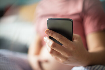Pregnant woman sitting on floor at home and using mobile phone.