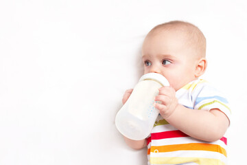 Caucasian baby boy with baby milk bottle on white blanket. Close up. Baby feeding and artificial...