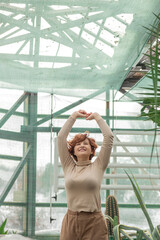 A beautiful plus size girl enjoying standing among the green plants of the greenhouse. Cottagecore style 