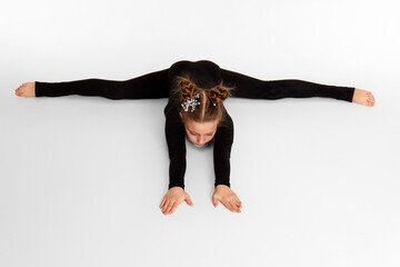 cute little child girl in black sportswear sitting on a transverse twine. Good stretching and gymnastics