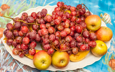 Pink grapes and apples on a white ceramic plate close up against a blue tablecloth