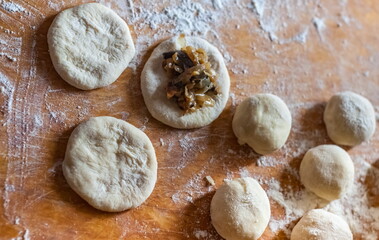 Balls of dough discs, a disk of dough stuffed with cabbage with mushrooms and wheat flour on a wooden cutting Board close-up