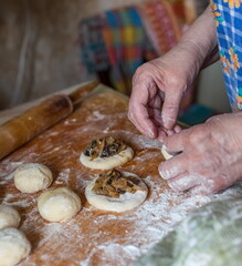 Dough balls, dough discs stuffed with cabbage with mushrooms, women's hands and wheat flour on a wooden cutting Board closeup