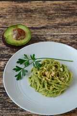 Gluten free chickpea spaghetti with avocado spinach pesto sauce garnish with parsley and pine nuts