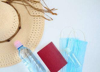 Straw hat, passport, face medical mask, bottle, hand sanitizer on white background with copy space. Preparing for travel in new normal. Personal protection, flight rules during coronavirus pandemic.