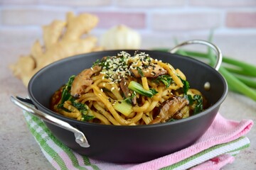 Stir-fried egg noodles in a wok with shiitake mushroom and bok choy garnish with white and black sesame seeds