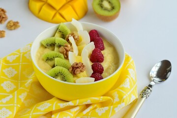 Mango banana pineapple smoothie bowl topped with raspberry, kiwi, walnut and coconut chips