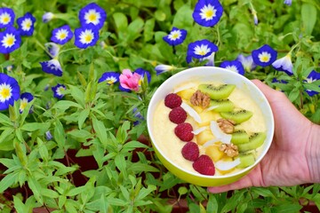 Mango banana pineapple smoothie bowl topped with raspberry, kiwi, walnut and coconut chips. Flower...