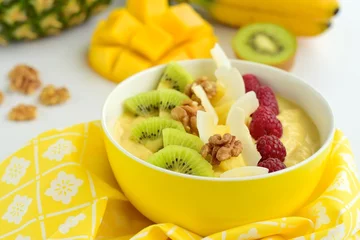 Fototapeten Mango banana pineapple smoothie bowl topped with raspberry, kiwi, walnut and coconut chips. Selective focus © AmalliaEka