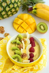Mango banana pineapple smoothie bowl topped with raspberry, kiwi, walnut and coconut chips