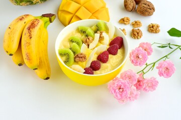 Mango banana pineapple smoothie bowl topped with raspberry, kiwi, walnut and coconut chips