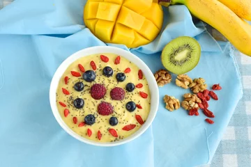 Foto auf Acrylglas Mango banana pineapple smoothie bowl topped with raspberry, blueberry, goji berry and chia seeds © AmalliaEka
