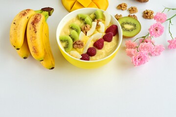 Mango banana pineapple smoothie bowl topped with raspberry, kiwi, walnut and coconut chips