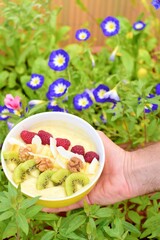 Mango banana pineapple smoothie bowl topped with raspberry, kiwi, walnut and coconut chips