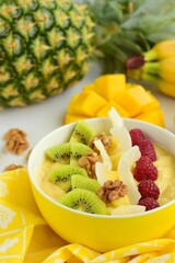 Mango banana pineapple smoothie bowl topped with raspberry, kiwi, walnut and coconut chips