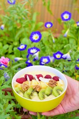Mango banana pineapple smoothie bowl topped with raspberry, kiwi, walnut and coconut chips