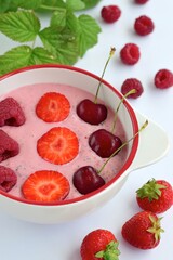 Breakfast berry smoothie bowl topped with raspberry, strawberry and cherry on white background