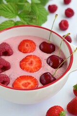 Breakfast berry smoothie bowl topped with raspberry, strawberry and cherry on white background