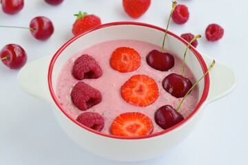 Breakfast berry smoothie bowl topped with raspberry, strawberry and cherry on white background
