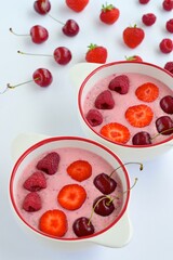 Breakfast berry smoothie bowl topped with raspberry, strawberry and cherry on white background