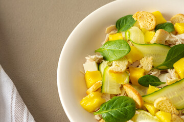 Plate with salad close-up on a brown background, salad of cucumber and chicken breast, mozzarella and croutons with sweet mango pieces and spinach