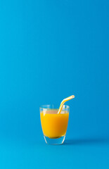 Delicious sweet orange or mango juice in glass with a straw isolated on blue background