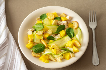 Plate with salad and fork close-up on a brown background, salad of cucumber and chicken breast, mozzarella and croutons with sweet mango pieces and spinach