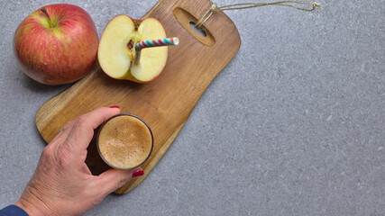 Zumo de manzana exprimida en un vaso con mano de mujer y sobre una tabla de cortar una manzana cortada con una pajita
