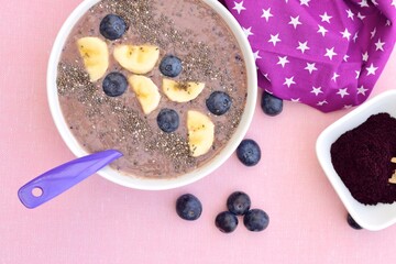 Acai berry smoothie bowl with banana, blueberry and chia seeds. Pink background. Top view
