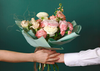 Man holding and giving a beautiful bouquet with flowers to woman on green background. Front view....