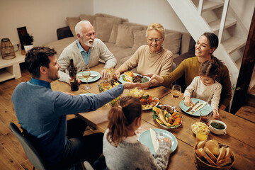 Happy couple passing food while having family lunch in dining room.