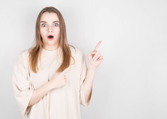 Image of surprised young lady standing isolated on gray background. Looking into the camera, pointing with two fingers.