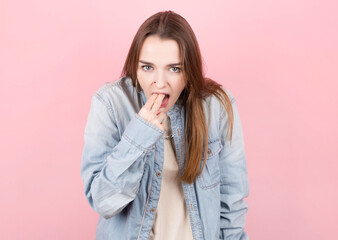 Portrait of disgusting woman in denim shirt showing disgust for bad smell or taste against pink background