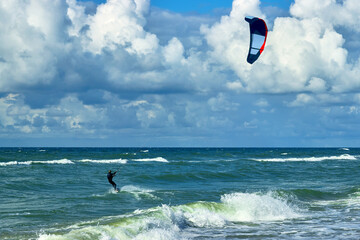 Kitesurfer on the crest of a wave. Blue sky with white clouds