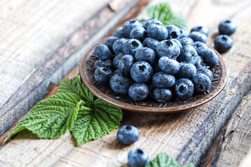 fresh juicy blueberries with green leaves in a plate on a wooden table. healthy berry, antioxidants, antiage foods