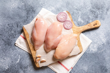 raw chicken breasts on a cutting board and on a gray concrete background with onion and garlic