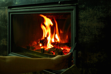 A man's hand puts wood in the burning fireplace. Modern closed fireplace with glass.
